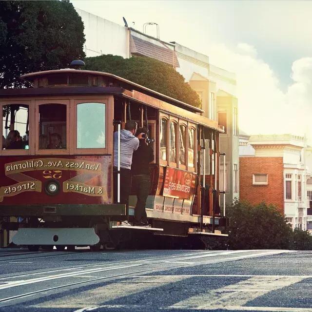 Una funivia gira attorno a una collina a San Francisco con i passeggeri che guardano fuori dal finestrino.