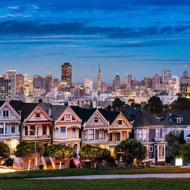 Die berühmten Painted Ladies vom Alamo Square sind in der Dämmerung vor der Skyline von San Francisco zu sehen.